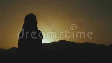 美丽的年轻女子在沙漠中日落时散步的<strong>剪影</strong>。 穿过沙漠，沙丘，风吹，缓慢